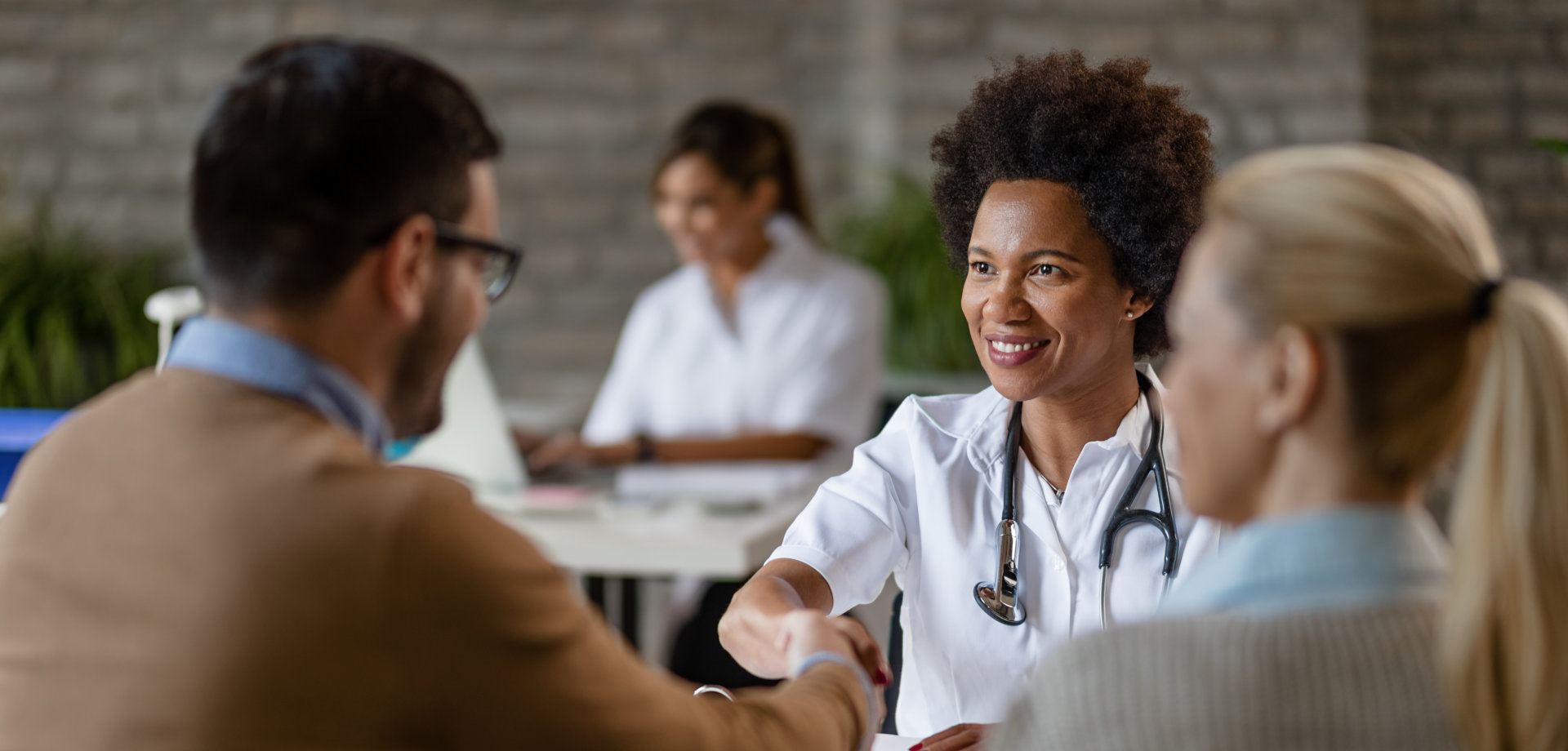 Happy African American doctor shaking hands with a couple at clinic.
