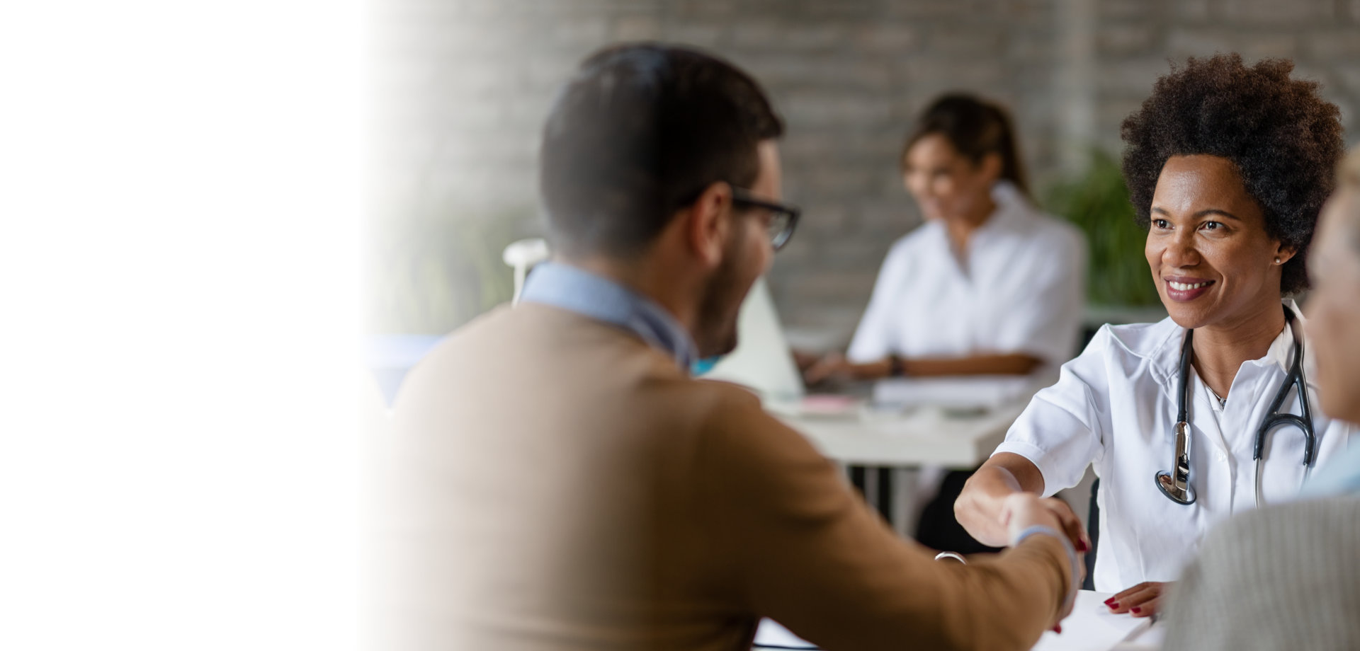 Happy African American doctor shaking hands with a couple at clinic.