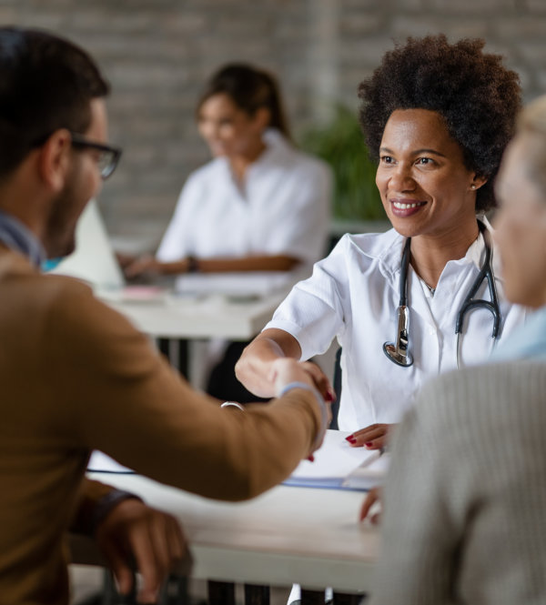 Happy African American doctor shaking hands with a couple at clinic.